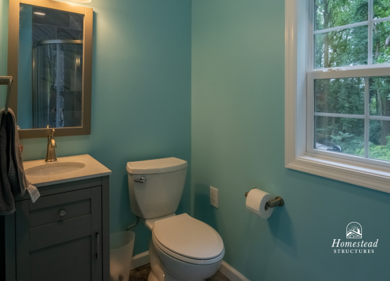 Brightly lit bathroom within a pool house featuring blue walls, contemporary vanity with sink, mirror, and toilet, designed for convenience and comfort.