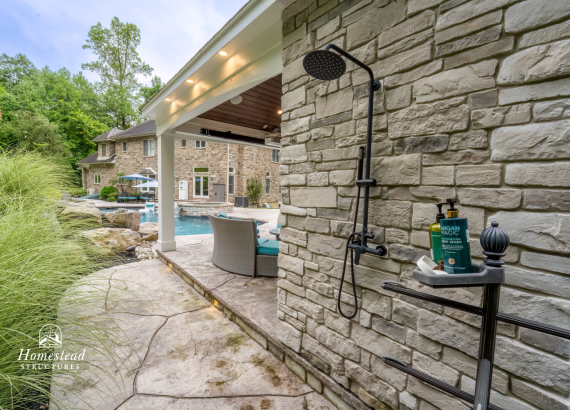 Stylish outdoor shower attached to a stone-clad pool house, seamlessly blending functionality with elegant backyard landscaping.