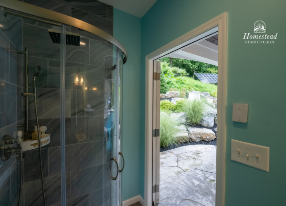Modern indoor shower with curved glass enclosure inside a pool house, featuring direct access to an outdoor pool and landscaped garden