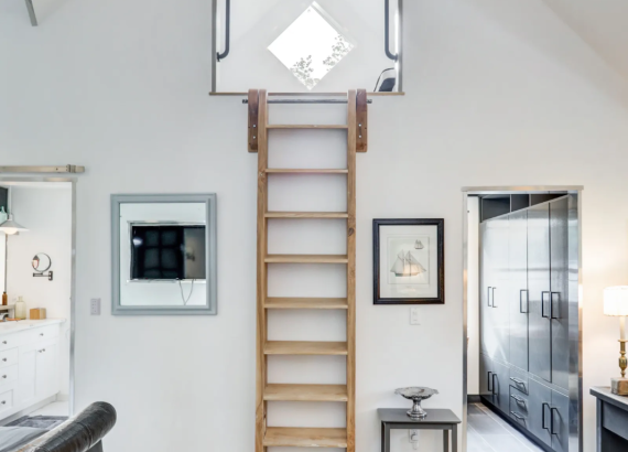 Close-up of a ladder leading to additional space, with nearby doors to a bathroom and office area in a custom two-story garage